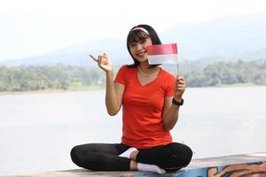 bellissimo giovane asiatico donna trasporto il indonesiano bandiera con un' allegro viso foto
