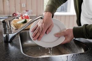 Uomini mani lavare un' bianca piatto dopo mangiare, sotto in esecuzione acqua, nel il lavello, nel il cucina. foto