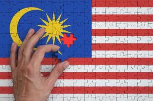 Malaysia bandiera è raffigurato su un' puzzle, quale il dell'uomo mano completa per piegare foto