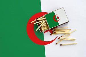 algeria bandiera è mostrato su un Aperto scatola di fiammiferi, a partire dal quale parecchi fiammiferi autunno e bugie su un' grande bandiera foto