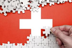 Svizzera bandiera è raffigurato su un' tavolo su quale il umano mano pieghe un' puzzle di bianca colore foto