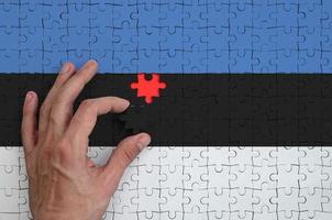Estonia bandiera è raffigurato su un' puzzle, quale il dell'uomo mano completa per piegare foto