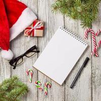 Natale e attività commerciale elementi con copia spazio ritagliata Santa berretto bloc notes penna bicchieri e decorato regalo scatola e abete albero foto