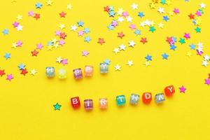iscrizione contento compleanno e multicolore coriandoli nel il modulo di stelle su giallo sfondo foto