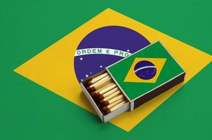 brasile bandiera è mostrato nel un Aperto scatola di fiammiferi, quale è pieno con fiammiferi e bugie su un' grande bandiera foto