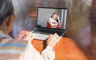 avvicinamento di moderno anziano donna seduta a casa, in linea computer consultazione, malato anziano donna parlando video chiamata con femmina infermiera utilizzando computer portatile, assistenza sanitaria concetto. foto