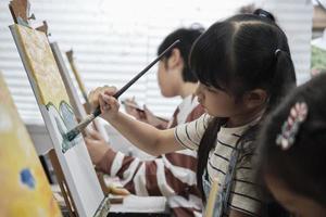 un' giovane asiatico ragazza si concentra su acrilico colore immagine pittura su tela con alunno bambini nel un arte aula, creativo apprendimento con talenti e abilità nel il elementare scuola studio formazione scolastica. foto