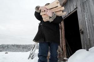 uomo, nel caldo Abiti, è venuto su di il fienile con un bracciata di legna da ardere, nel il campagna. riscaldamento stagione nel il villaggio. foto