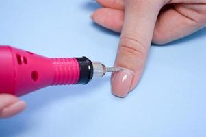 il processi di fabbricazione un' bellissimo manicure su il dita di un' dito in lavorazione un' chiodo con un' speciale macchina nel un' chiodo bellezza salone su un' blu sfondo foto