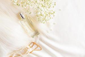 superiore Visualizza di un' elegante bottiglia di Da donna profumo su un' pastello raso tessuto sfondo con perle e un' gypsophila ramo. pubblicità concetto.