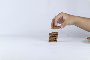 mani impilamento biscotti su un' bianca sfondo. umano mano assunzione avena biscotto a partire dal un' pila foto