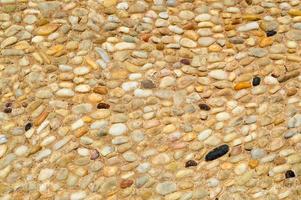 struttura di un' pietra parete, strade a partire dal piccolo il giro e ovale pietre con sabbia con cuciture di naturale vecchio giallo nero Marrone. il sfondo foto