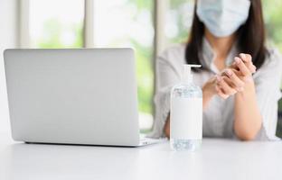 bottiglia di gel di alcol con una donna che indossa la maschera per il viso lavandosi la mano foto