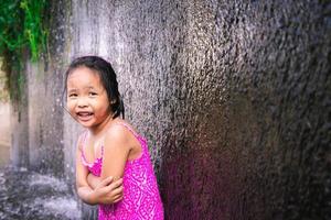 felice piccola ragazza asiatica che gioca in acqua foto