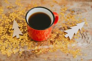 oro scintillii, di legno Natale alberi e un' tazza con caffè su un' di legno sfondo. Natale sfondo fatto di scintille e rosso tazze con caffè. accogliente e caldo tiro con caldo caffè foto