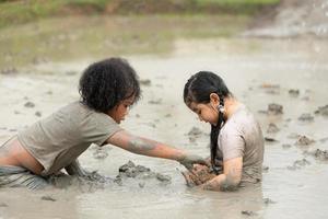 bambini avere divertimento giocando nel il fango nel il Comunità i campi e attraente un' rana nel un' fangoso campo. foto