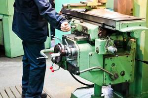 un' maschio lavoratore lavori su un' più grandi metallo ferro fabbro ferraio tornio, attrezzatura per riparazioni, metallo opera nel un' laboratorio a un' metallurgico pianta nel un' riparazione produzione foto