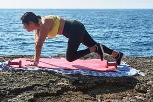 latino donna, di mezza età, indossare abbigliamento sportivo, addestramento, fare fisico esercizi, tavola, sit-up, quello dello scalatore fare un passo, ardente calorie, conservazione in forma, all'aperto di il mare, indossare cuffia, inteligente orologio foto