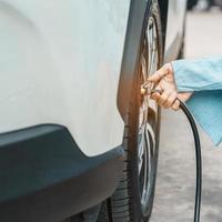 donna conducente che gonfia a mano i pneumatici del veicolo, rimuovendo il tappo di azoto della valvola del pneumatico per controllare la pressione dell'aria e riempire l'aria sulla ruota dell'auto alla stazione di servizio. self service, manutenzione e sicurezza foto