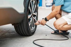 uomo guidatore che gonfia a mano i pneumatici del veicolo, rimuovendo il tappo di azoto della valvola del pneumatico per controllare la pressione dell'aria e riempire l'aria sulla ruota dell'auto alla stazione di servizio. self service, manutenzione e sicurezza foto