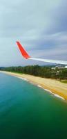 rosso e grigio o grigio ala di aereo volante su il spiaggia con mare o oceano, albero, cielo e bianca nube. aereo viaggio per destinazione e trasporto concetto. aereo o superiore Visualizza di aereo su aria. foto