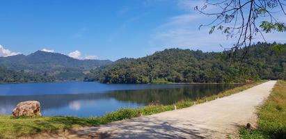 strada o strada accanto lago o fiume con verde montagna e blu cielo sfondo a huai bon serbatoio chiang mai, Tailandia. tra natura con riflessione su acqua e copia spazio. bellezza nel natura foto