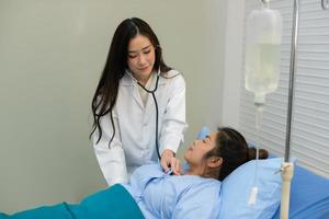 sorridente asiatico femmina medico utilizzando stetoscopio ascoltando controllo battito cardiaco Grasso donna paziente su il letto, visita medica e diagnosi. foto