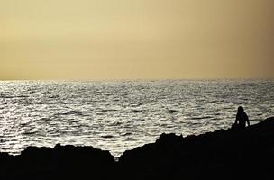 silhouette di persona seduta sulla riva dell'oceano foto