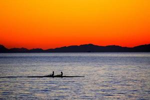 silhouette di due persone su barche a remi durante il tramonto foto