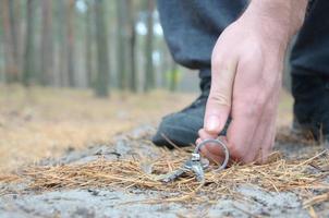 maschio mano raccolta su perso chiavi a partire dal un' terra nel autunno abete legna sentiero. il concetto di scoperta un' prezioso cosa e bene fortuna foto