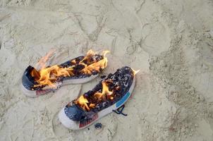 ardente gli sport scarpe da ginnastica o Palestra scarpe su fuoco In piedi su sabbioso spiaggia costa. atleta bruciato fuori. fisico sforzo durante formazione concetto foto