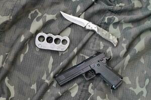 pistola bugie con ottone nocche e coltello su camuffare militare uniforme vicino su. concetto di saccheggio e braccia commercio foto