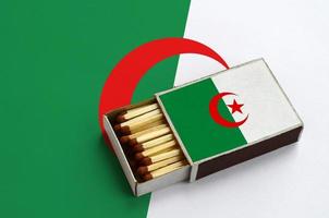 algeria bandiera è mostrato nel un Aperto scatola di fiammiferi, quale è pieno con fiammiferi e bugie su un' grande bandiera foto