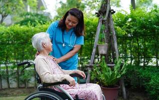 il medico aiuta il paziente asiatico della disabilità della donna anziana che si siede sulla sedia a rotelle nel parco, concetto medico. foto