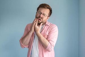 uomo con bicchieri è sperimentare un' acuto mal di denti, mantiene mano su guancia e si chiude occhi nel sofferenza. medico concetto. foto