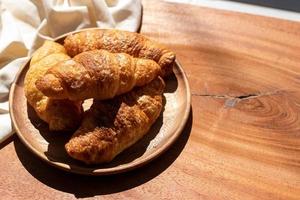 brioche nel di legno piatto, bianca stoffa, mattina luce del sole foto