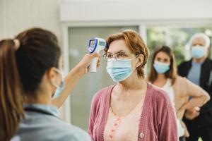 anziano donna avendo sua temperatura verificato prima covid-19 vaccino foto