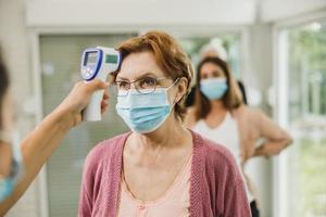 anziano donna avendo sua temperatura verificato prima covid-19 vaccino foto