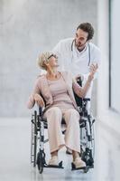 medico spingendo il suo anziano femmina paziente nel un' sedia a rotelle lungo il ospedale corridoio foto
