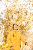 ragazzo nel un' giallo giacca, disperde le foglie nel un autunno parco. il bambino gioisce nel il autunno le foglie. contento infanzia. luminosa giallo giacca e le foglie foto