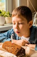 ragazzo di 9 anni vecchio colpi su il candela su il torta. festeggiare compleanno a casa. casa vacanza per bambini. ritratto di un' ragazzo soffiaggio su un' candela. rendere un' desiderio. compimento di desideri foto