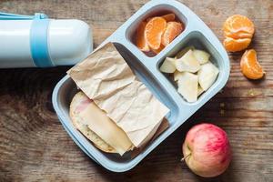 scolaro pranzo scatola con thermos su di legno sfondo.mela,mandarino,sandwich nel sacco per il pranzo e acqua bottiglia foto