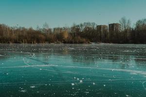 congelato lago, cerchi su il ghiaccio nel il parco, contro il fondale di il foresta e il città foto