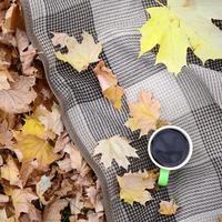 autunno le foglie e caldo cottura a vapore tazza di caffè bugie su scacchi plaid all'aperto foto