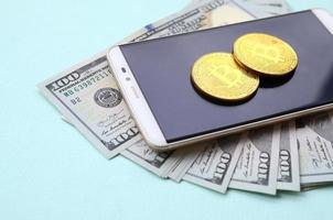 bitcoin bugie su un' smartphone e centinaio dollaro fatture su un' leggero blu sfondo foto