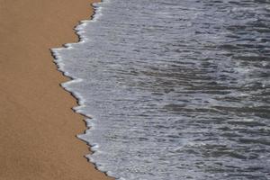 schiuma a partire dal il onde come essi raggiungere il sabbia su il spiaggia foto
