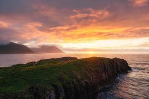 tramonto al di sopra di montagna capo con pulcinelle di mare colonia nel estate su orientale a borgarfjardarhofn, Islanda foto