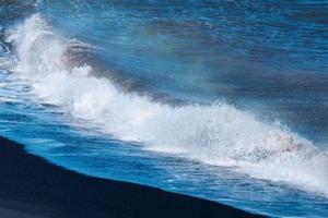 blu oceano onda con spruzzi colpire su nero sabbia spiaggia nel estate foto