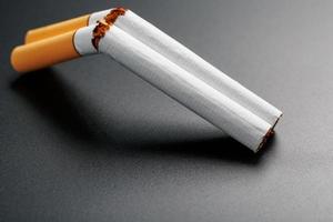 Due sigarette nel il modulo di un' doppia canna fucile da caccia su un' nero sfondo con copia spazio. fermare fumare. il concetto di fumo uccide. foto