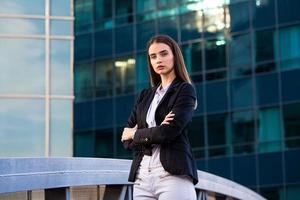 attività commerciale donna con attraversato braccia. fiducioso moderno attività commerciale donna in piedi vicino un' grande finestre neer sua ufficio. foto